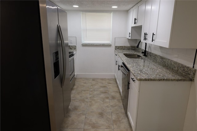 kitchen featuring sink, light stone counters, a textured ceiling, appliances with stainless steel finishes, and white cabinets