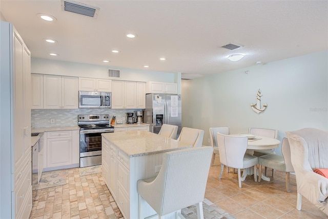 kitchen featuring a kitchen island, appliances with stainless steel finishes, white cabinetry, decorative backsplash, and light stone countertops