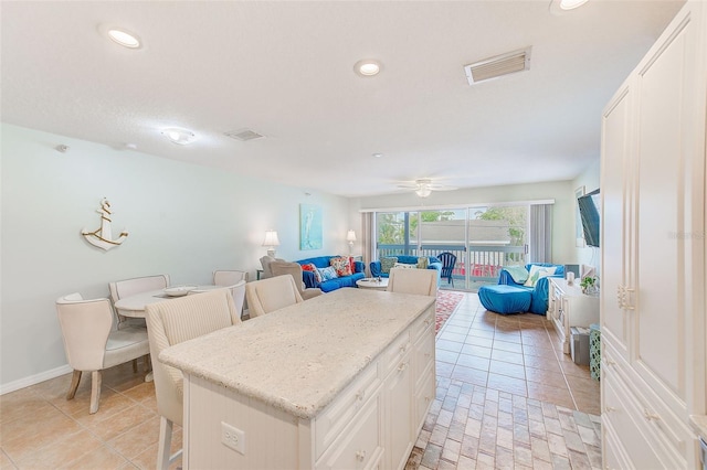 kitchen with light tile patterned floors, ceiling fan, a kitchen breakfast bar, white cabinets, and a kitchen island