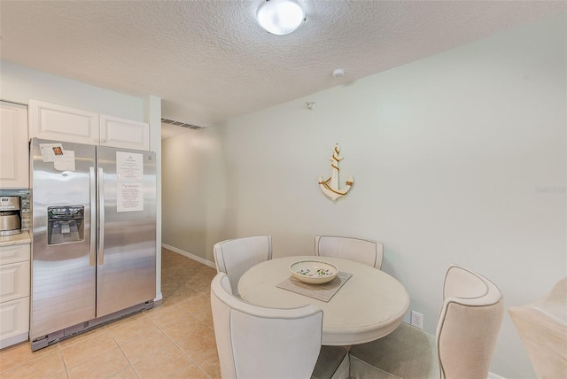 dining room featuring light tile patterned floors, baseboards, visible vents, and a textured ceiling