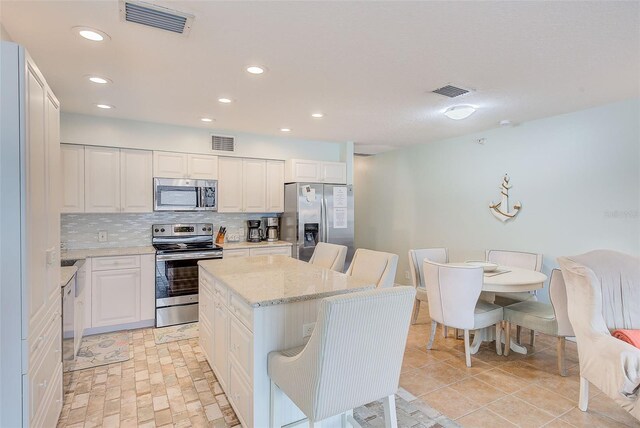 kitchen with appliances with stainless steel finishes, white cabinets, a kitchen island, and visible vents