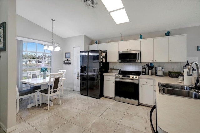 kitchen featuring lofted ceiling, sink, decorative light fixtures, appliances with stainless steel finishes, and white cabinets