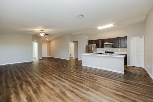 kitchen with ceiling fan, a kitchen island with sink, stainless steel appliances, dark hardwood / wood-style floors, and dark brown cabinetry