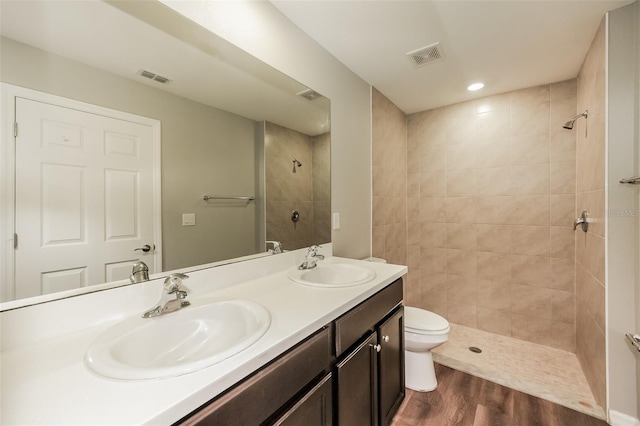 bathroom featuring hardwood / wood-style flooring, vanity, toilet, and a tile shower