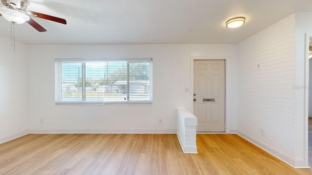 empty room with light hardwood / wood-style floors, ceiling fan, and brick wall