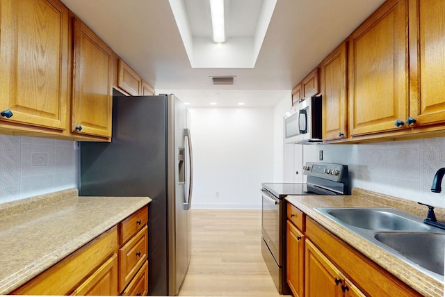 kitchen featuring a raised ceiling, tasteful backsplash, sink, stainless steel appliances, and light hardwood / wood-style flooring