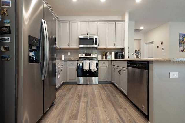 kitchen with appliances with stainless steel finishes, wood finished floors, a peninsula, gray cabinetry, and backsplash