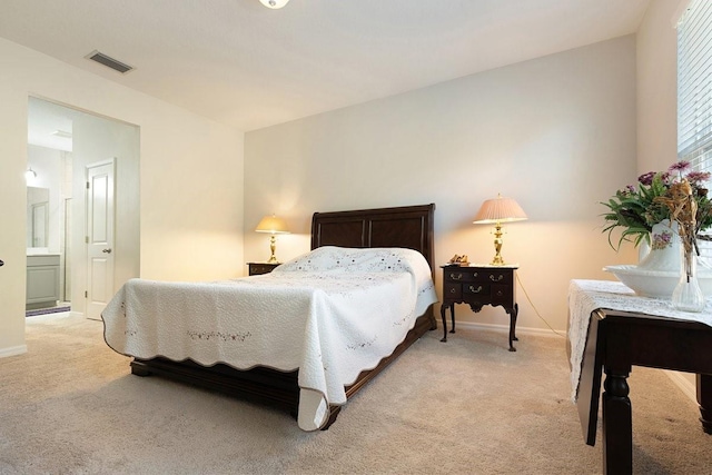 bedroom with light carpet, visible vents, baseboards, and ensuite bathroom