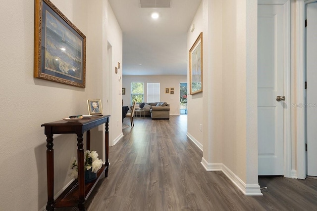 hall featuring visible vents, baseboards, and dark wood-style flooring