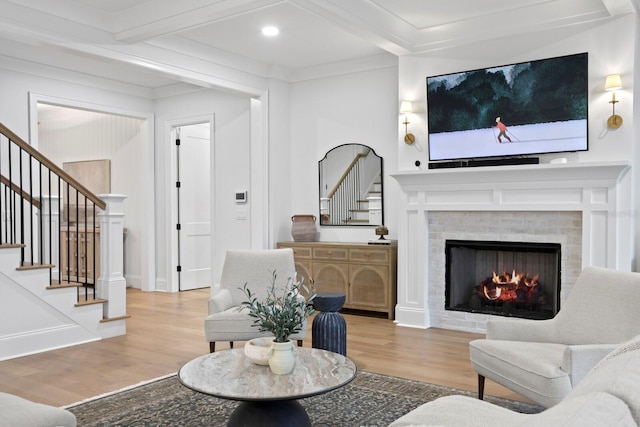 living room with beamed ceiling, ornamental molding, a fireplace, and light wood-type flooring