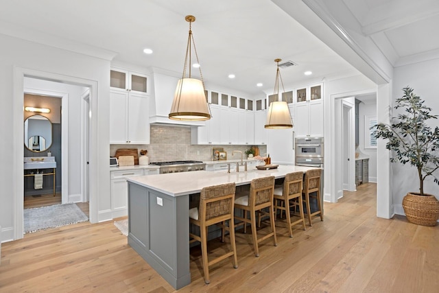 kitchen featuring pendant lighting, white cabinetry, a kitchen island with sink, and light hardwood / wood-style flooring