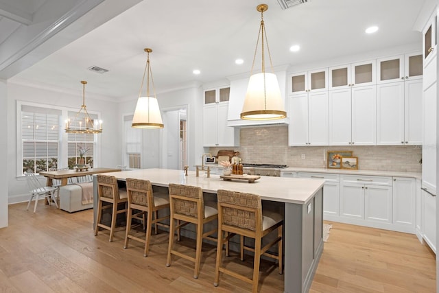 kitchen with white cabinets, a kitchen breakfast bar, hanging light fixtures, a kitchen island with sink, and light hardwood / wood-style floors