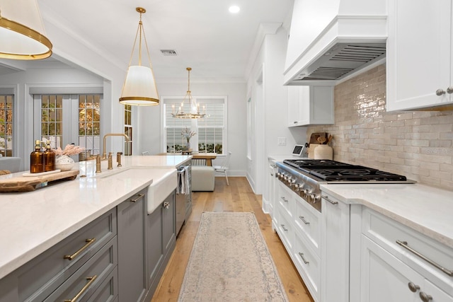 kitchen with gray cabinetry, white cabinetry, decorative light fixtures, custom range hood, and stainless steel gas stovetop