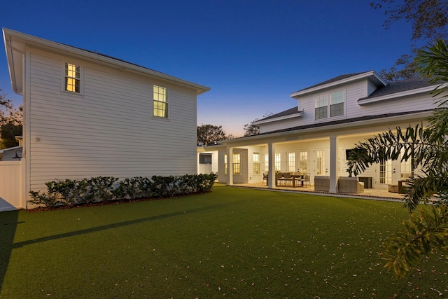 back house at dusk with a patio and a lawn