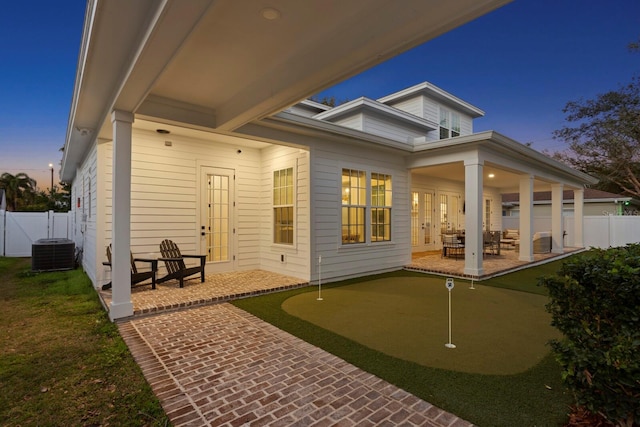 back house at dusk featuring central AC unit and a patio