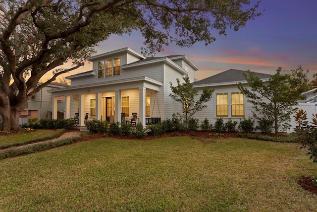 back house at dusk featuring a porch and a yard