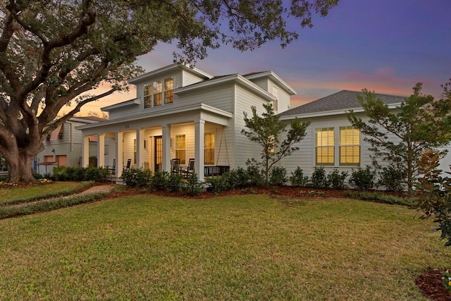 back house at dusk featuring a yard and a porch