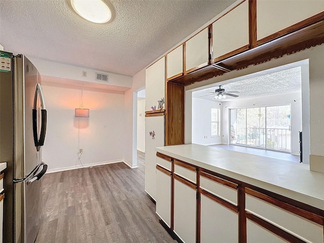 kitchen featuring white cabinetry, stainless steel refrigerator, a textured ceiling, and light wood-type flooring