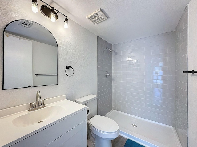 bathroom featuring vanity, a tile shower, a textured ceiling, and toilet