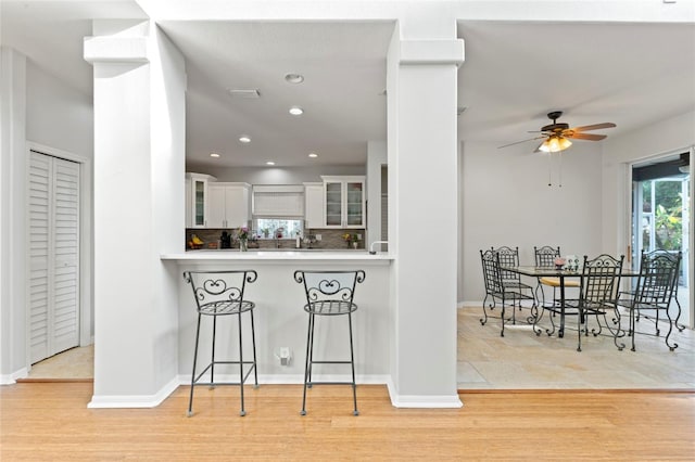 kitchen featuring a breakfast bar, white cabinetry, light hardwood / wood-style flooring, kitchen peninsula, and decorative backsplash