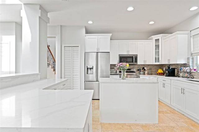 kitchen featuring appliances with stainless steel finishes, white cabinetry, light stone counters, a kitchen island, and decorative backsplash