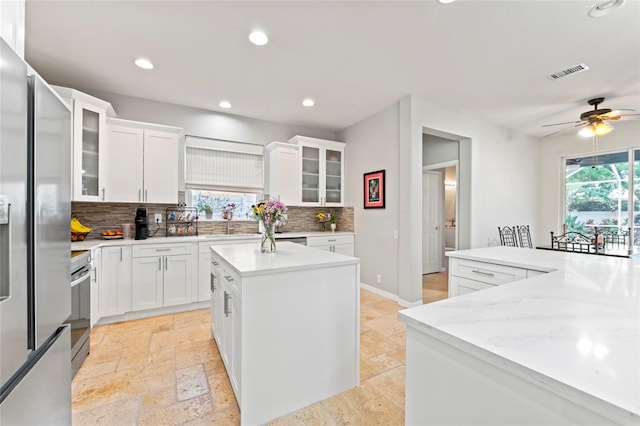 kitchen featuring sink, white cabinetry, light stone counters, a center island, and appliances with stainless steel finishes