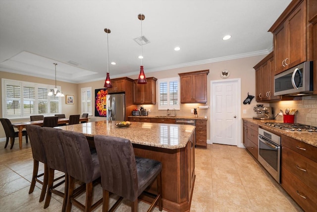 kitchen featuring pendant lighting, a kitchen island, light stone countertops, and appliances with stainless steel finishes