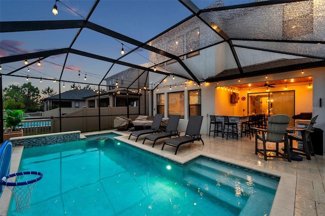 pool at dusk featuring ceiling fan, exterior bar, a patio area, and a lanai