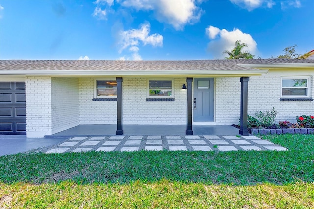 doorway to property with a garage, brick siding, and roof with shingles