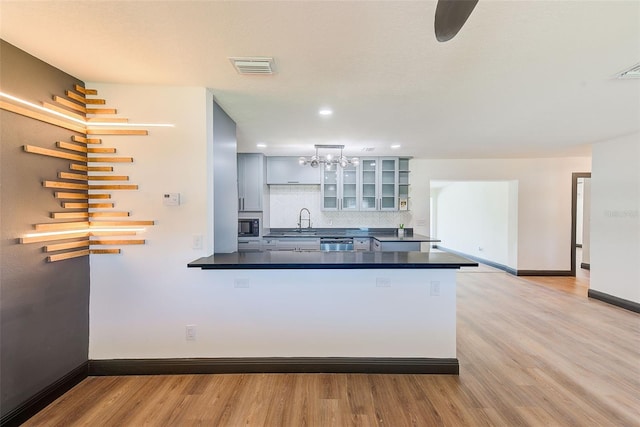 kitchen with a peninsula, a sink, light wood-style floors, backsplash, and dark countertops