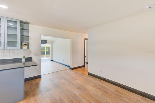 interior space featuring light wood-type flooring, dark countertops, glass insert cabinets, and baseboards