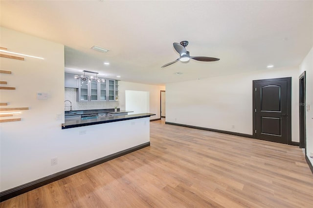 kitchen with baseboards, decorative backsplash, glass insert cabinets, light wood-type flooring, and a sink