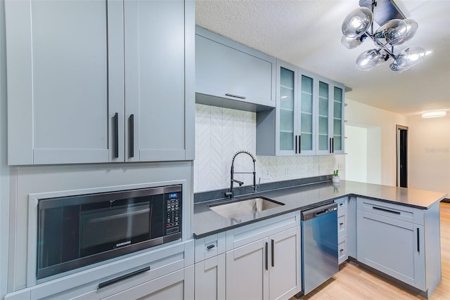 kitchen with a peninsula, a sink, appliances with stainless steel finishes, dark countertops, and glass insert cabinets