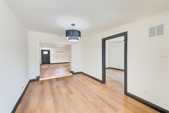 empty room with light wood-style floors, baseboards, and visible vents