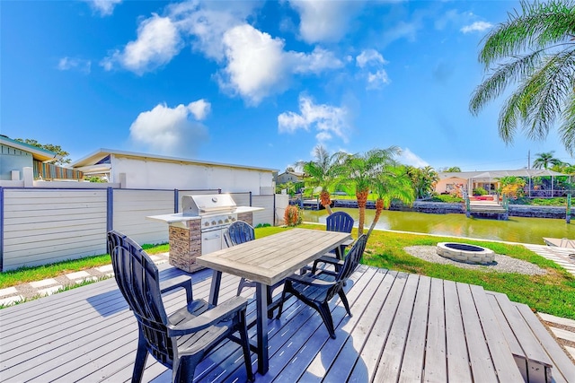 wooden deck with a water view, a yard, a fire pit, and outdoor dining space