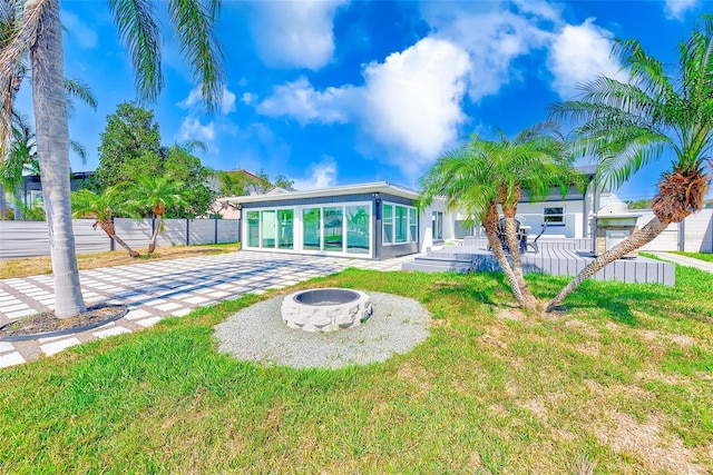 back of house featuring a sunroom, an outdoor fire pit, fence, and a yard