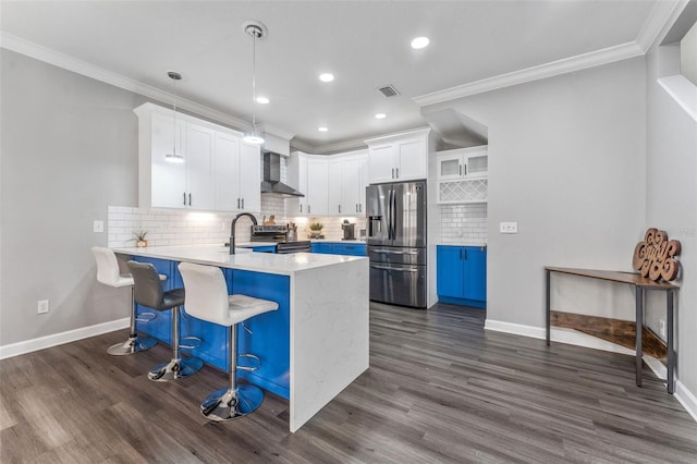 kitchen with stainless steel appliances, a kitchen bar, wall chimney range hood, and white cabinets