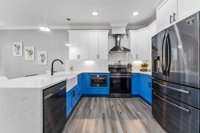 kitchen featuring wall chimney exhaust hood, blue cabinets, white cabinetry, appliances with stainless steel finishes, and pendant lighting