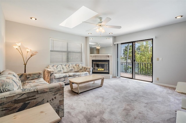 carpeted living room with ceiling fan, a tiled fireplace, and a skylight