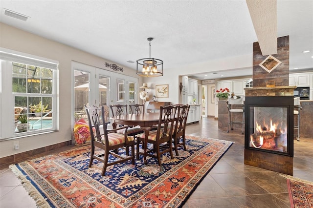 tiled dining space with a multi sided fireplace, a textured ceiling, and a notable chandelier