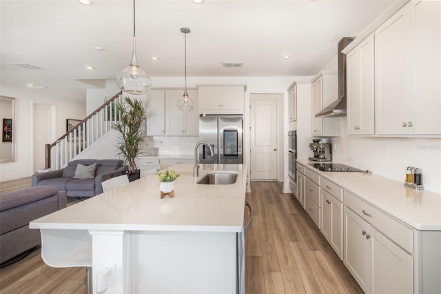 kitchen with appliances with stainless steel finishes, pendant lighting, sink, white cabinets, and wall chimney exhaust hood