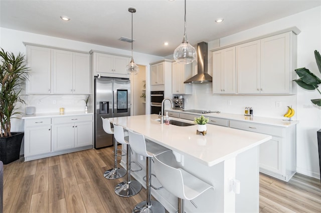 kitchen featuring sink, hanging light fixtures, black appliances, an island with sink, and wall chimney exhaust hood