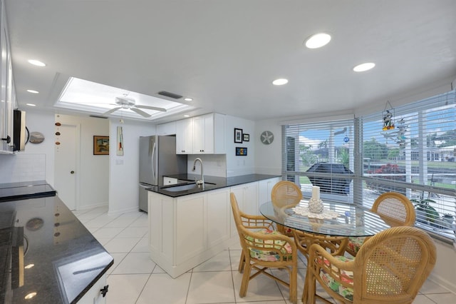 kitchen with stainless steel refrigerator, a skylight, white cabinetry, light tile patterned floors, and kitchen peninsula