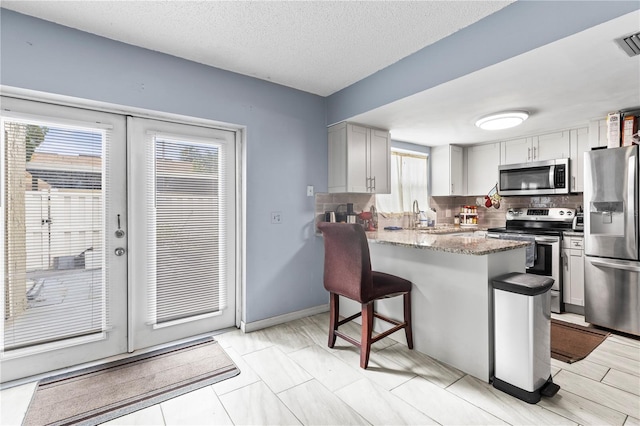 kitchen with appliances with stainless steel finishes, tasteful backsplash, kitchen peninsula, a textured ceiling, and french doors