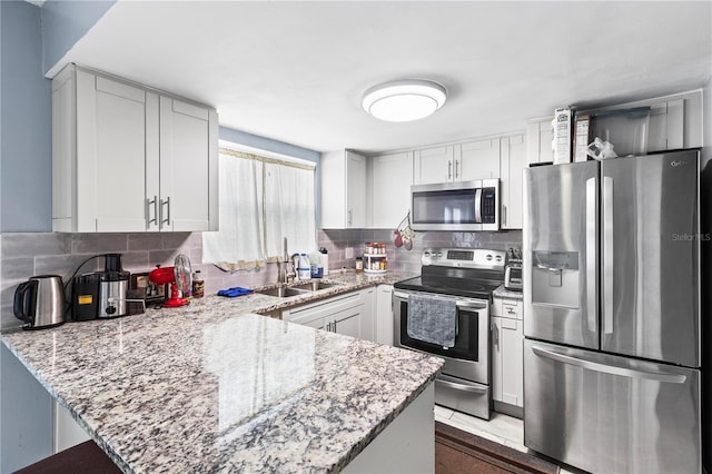 kitchen with tasteful backsplash, white cabinetry, kitchen peninsula, stainless steel appliances, and light stone countertops