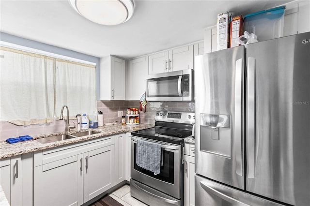 kitchen featuring sink, light stone counters, stainless steel appliances, decorative backsplash, and white cabinets