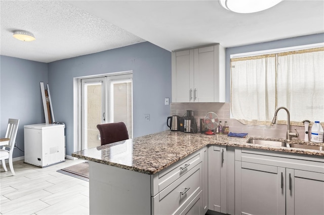 kitchen featuring sink, refrigerator, a textured ceiling, kitchen peninsula, and dark stone counters