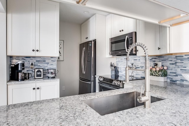 kitchen with light stone countertops, decorative backsplash, stainless steel appliances, and white cabinets