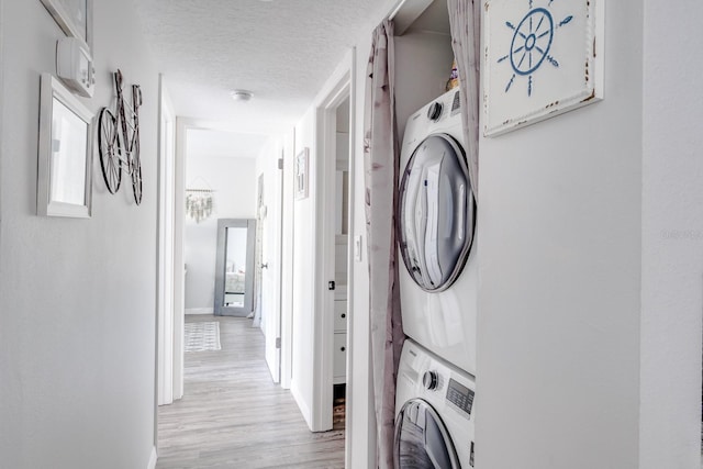 clothes washing area featuring stacked washer and dryer, a textured ceiling, and light hardwood / wood-style floors