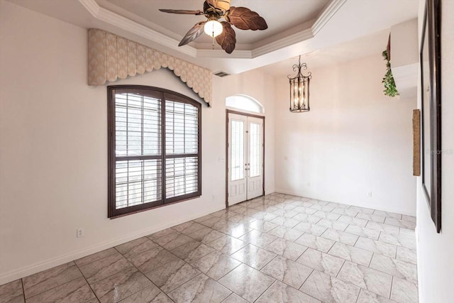 spare room featuring a tray ceiling, crown molding, ceiling fan with notable chandelier, and french doors